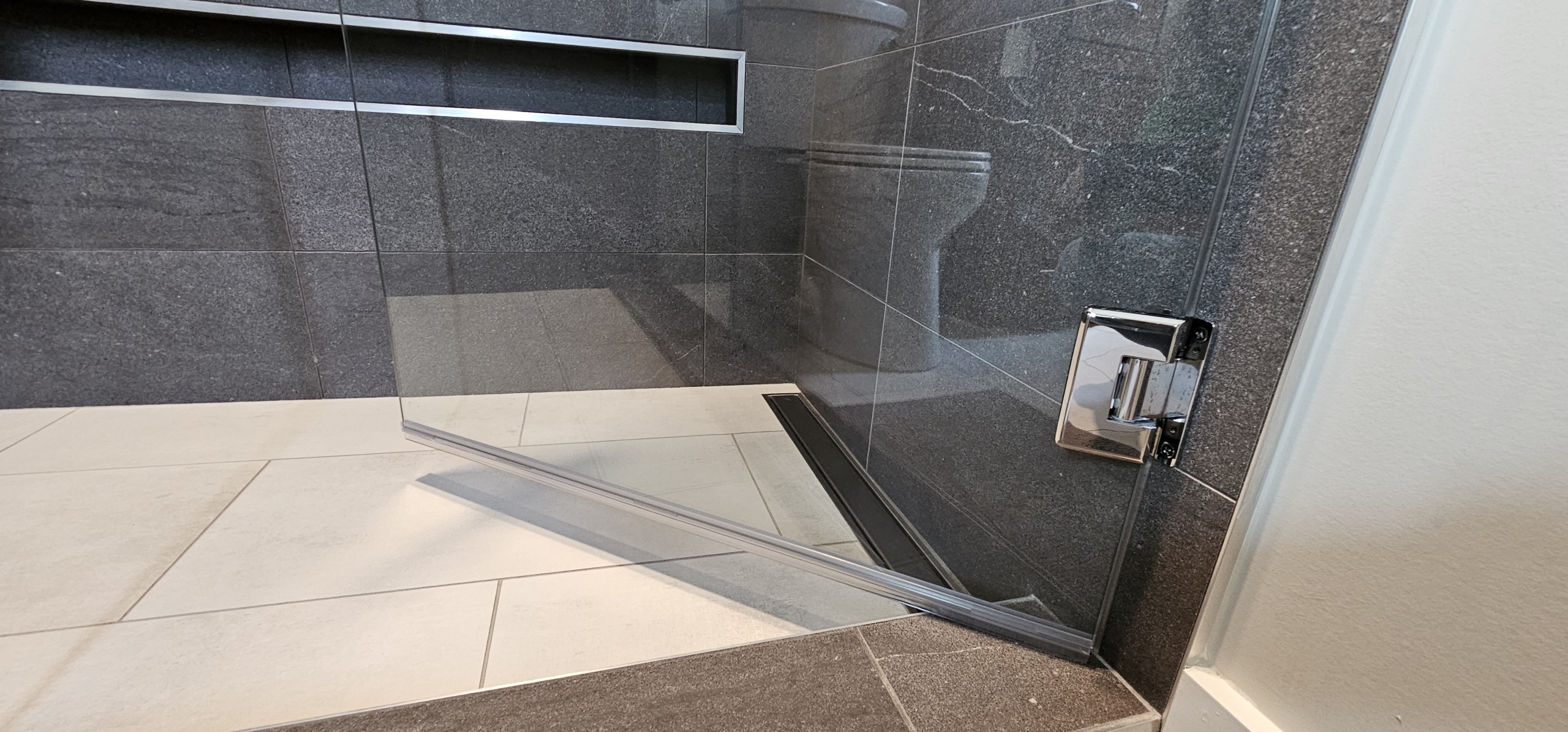 detail image of tile shower niche and glass shower door hinge
